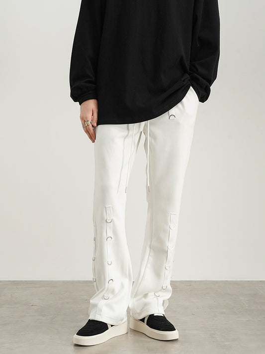 Person wearing a black oversized sweatshirt and white pants with button details on a plain background