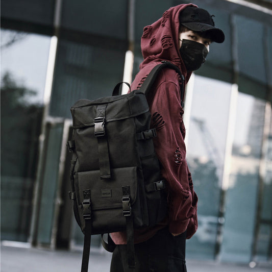 Person wearing a maroon hoodie and black backpack in front of a modern building.