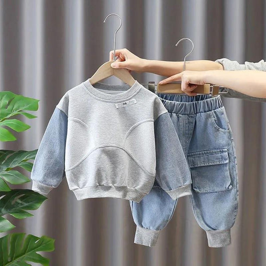 Children's gray sweatshirt and blue jeans set on hangers against a neutral background.