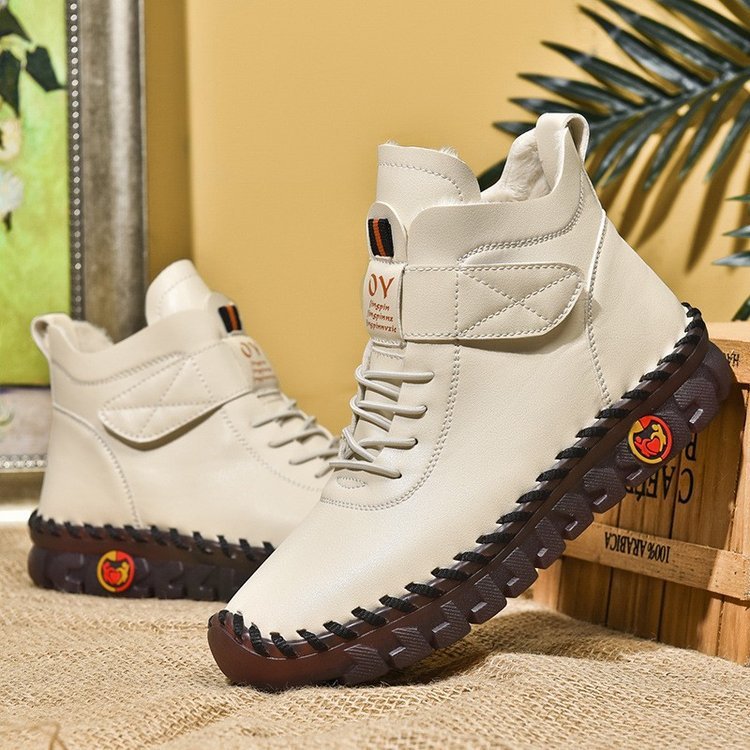 White high-top boots with brown soles on a textured surface with a plant in the background