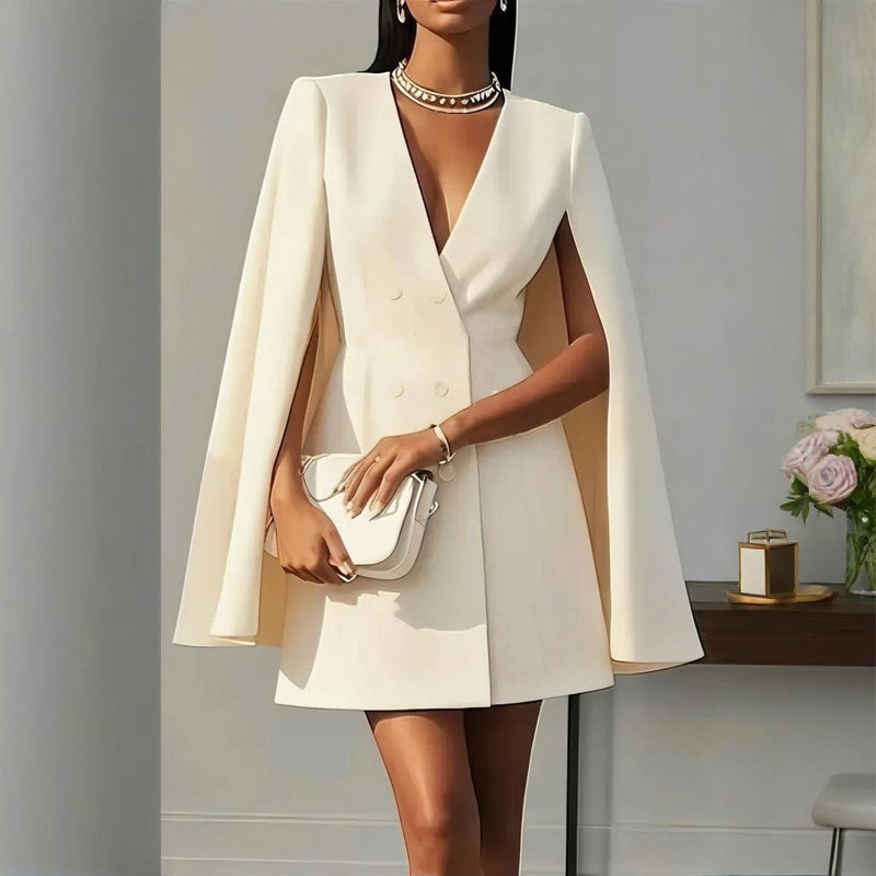 Woman wearing a white cape dress holding a clutch in an indoor setting.