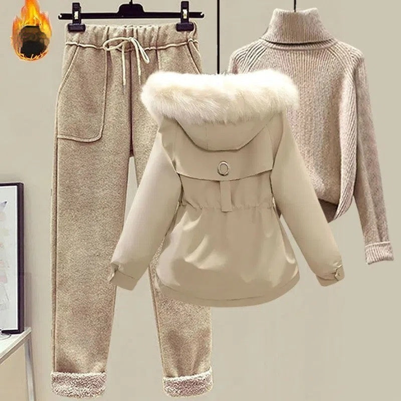 Beige winter coat with fur hood, matching pants, and a sweater on mannequins against a neutral background.
