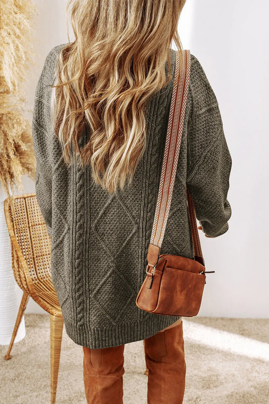 Person wearing a green cable knit sweater and brown leather bag indoors.