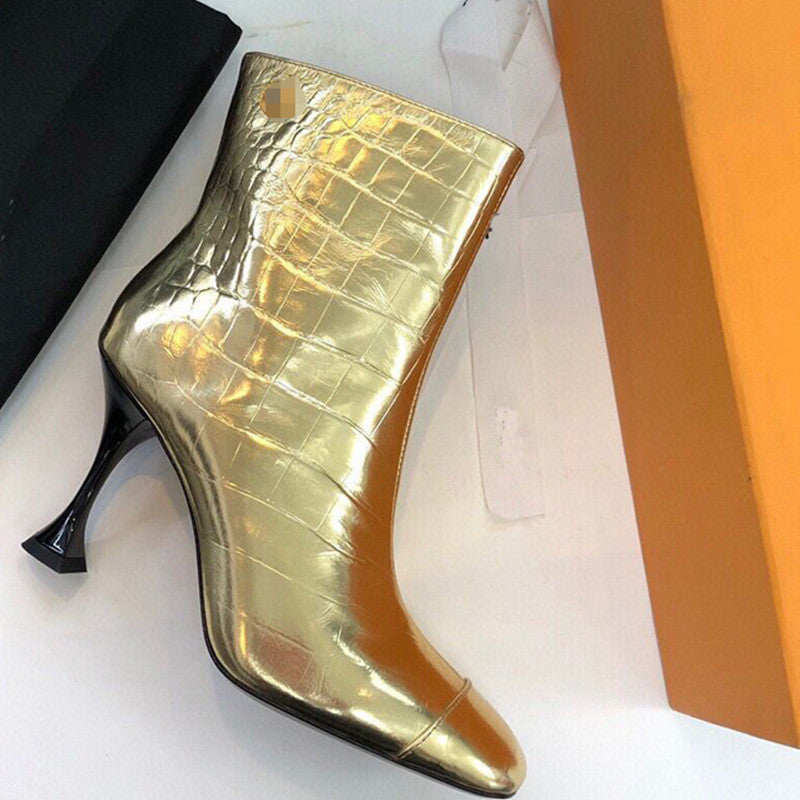 Gold high-heeled boot on a white surface with an orange box in the background