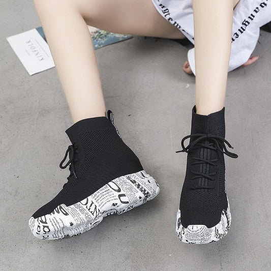 Black high-top sneakers with white sole design on a gray floor.