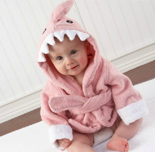 Baby wearing a pink shark-themed robe sitting on a white surface.