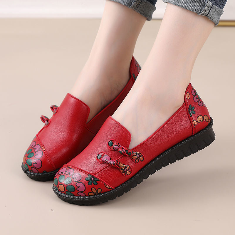 Red loafers with floral patterns worn by a person on a beige background