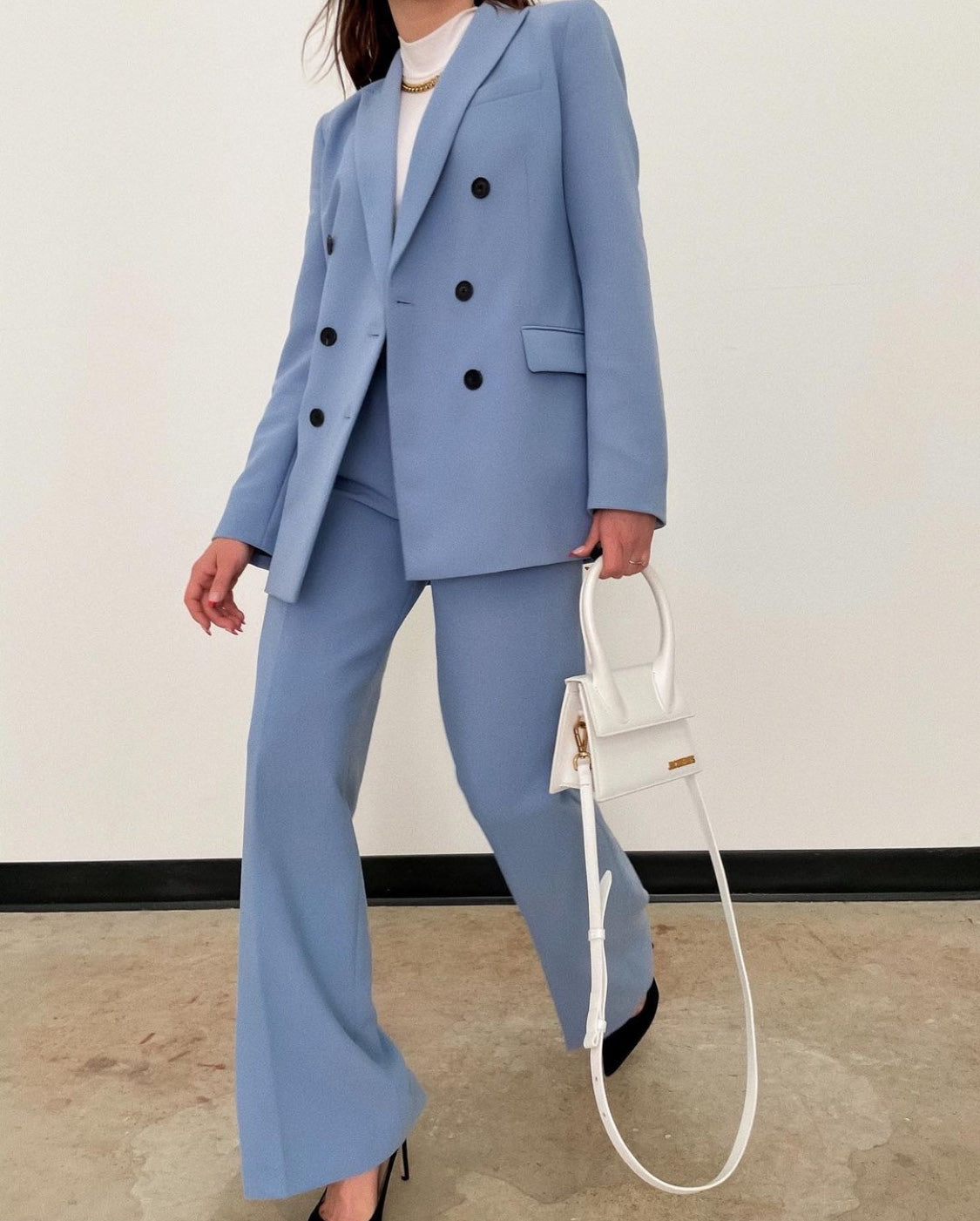 Person wearing a light blue suit holding a white handbag against a plain background by millivan