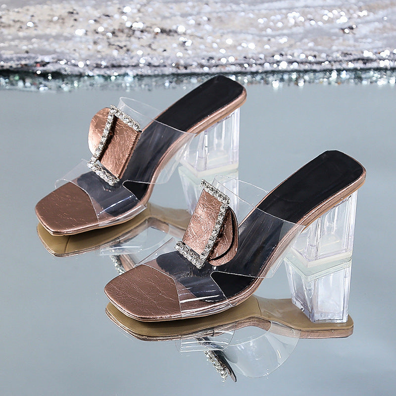 Bronze high-heeled shoes with clear plastic heels on a reflective surface.