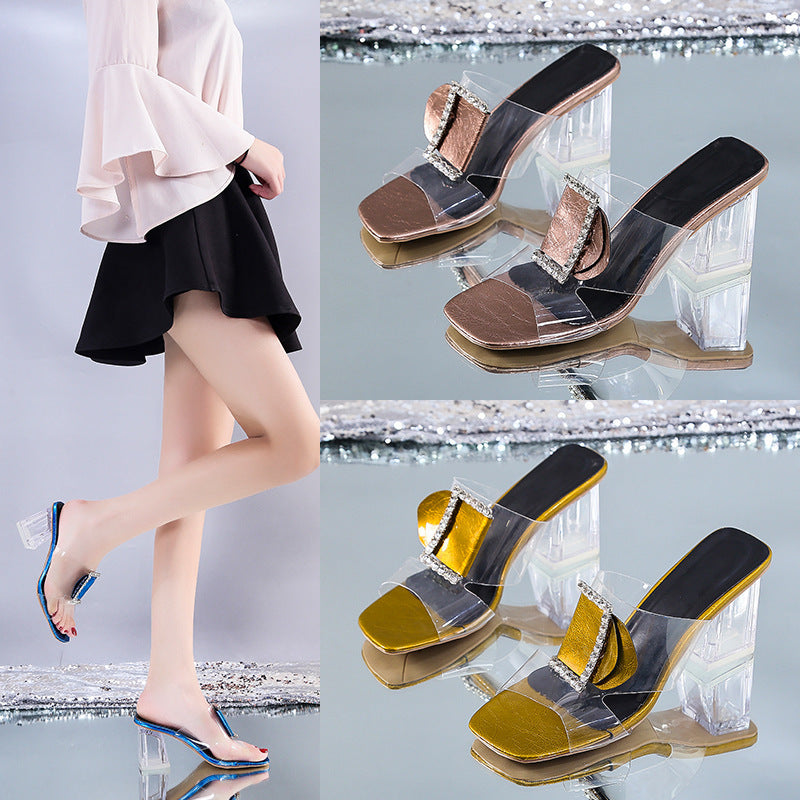 Transparent high-heeled shoes with gold and black accents worn by a person on a reflective surface.