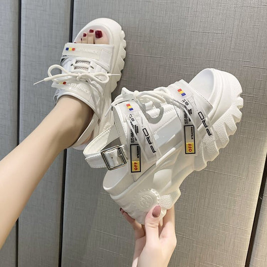 White sneakers with various labels held by a person against a gray background
