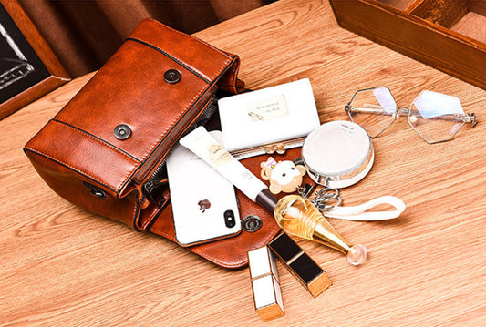 Brown leather bag with various items including a phone, wallet, and lipsticks on a wooden surface.