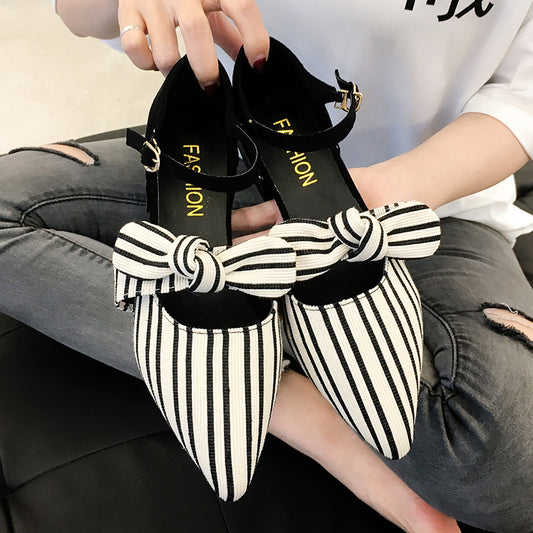 Black and white striped shoes with large bows worn by a person sitting on a couch.