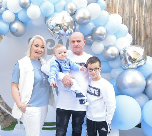 Family of four posing in front of a balloon arch with blue and silver balloons.