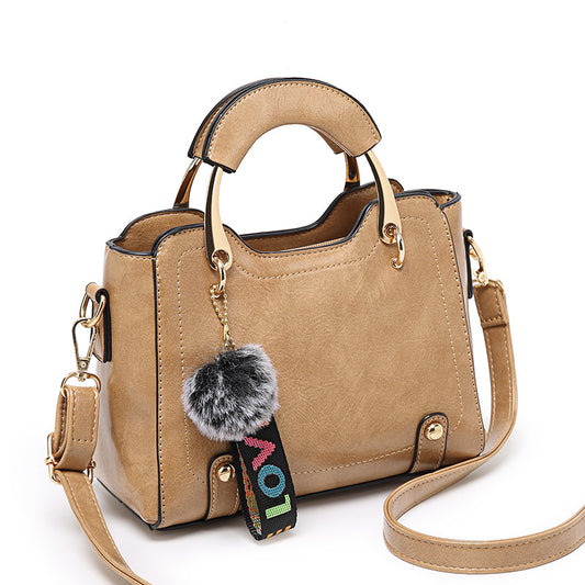 Beige handbag with a decorative keychain on a white background
