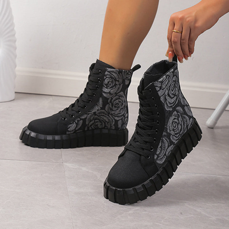 Black boots with rose pattern worn by a person on a light wooden floor.