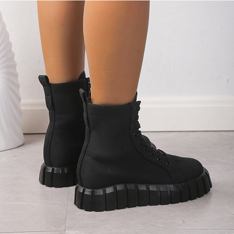 Black combat boots worn by a person on a light wooden floor.