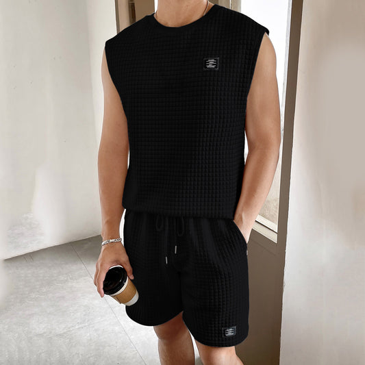 Person wearing a black sleeveless shirt and shorts set, holding a coffee cup.