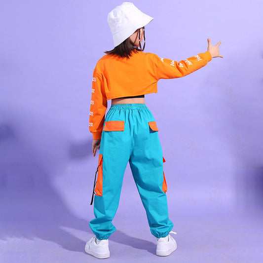 Person wearing an orange long-sleeve crop top and turquoise pants with white sneakers on a purple background
