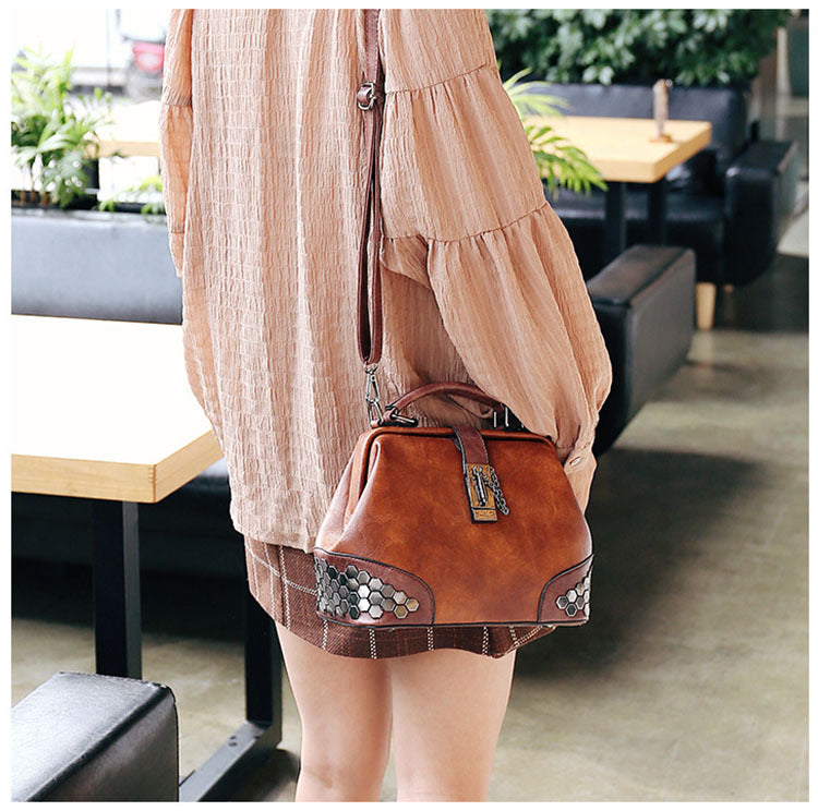 Person wearing a brown leather handbag with decorative elements in an indoor setting.