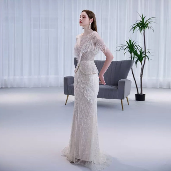 Woman in a white evening gown standing in a modern room with a gray sofa and plant.