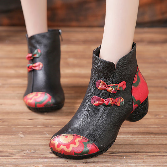 Black ankle boots with red and green floral patterns on a wooden floor.