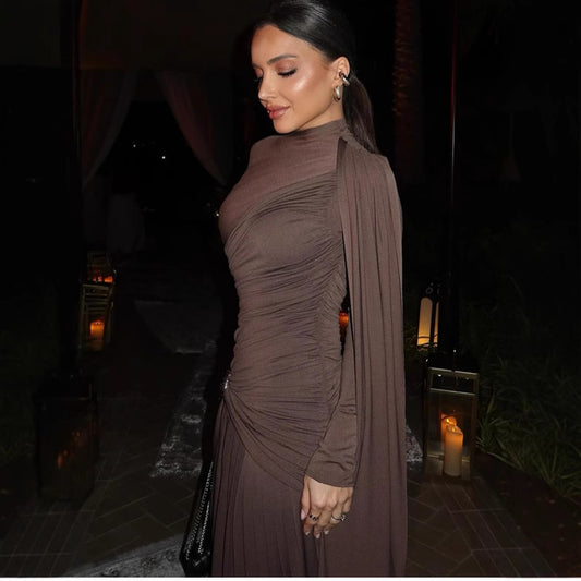 Woman in a brown dress standing in a dimly lit outdoor setting with candles.
