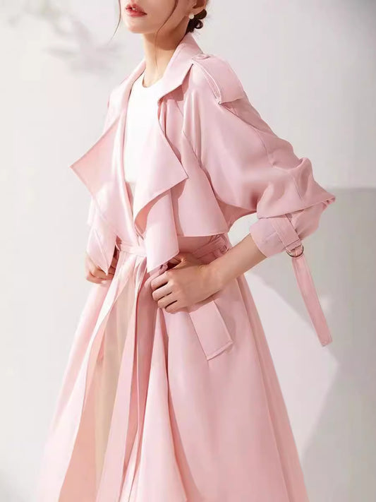 Person wearing a pink trench coat on a plain background