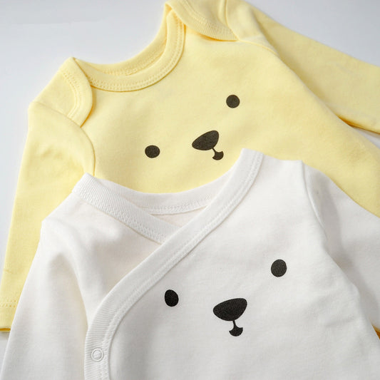 Two baby onesies with bear face designs, one yellow and one white, on a light gray background.
