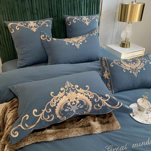 Blue bedding set with gold embroidery on a bed in a bedroom setting.