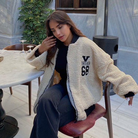 Woman sitting outdoors wearing a beige sherpa jacket with text
