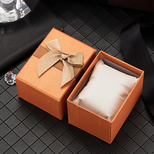Orange jewelry box with a beige bow on a black textured surface