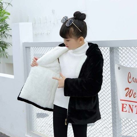 Child wearing a black coat with white lining, standing indoors against a white wall.