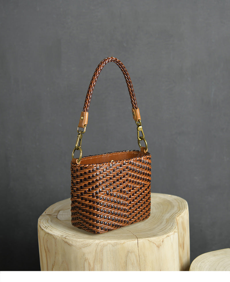 Brown woven handbag with braided handle on a wooden block against a gray background