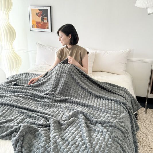 Woman sitting on a bed with a large gray blanket draped over her