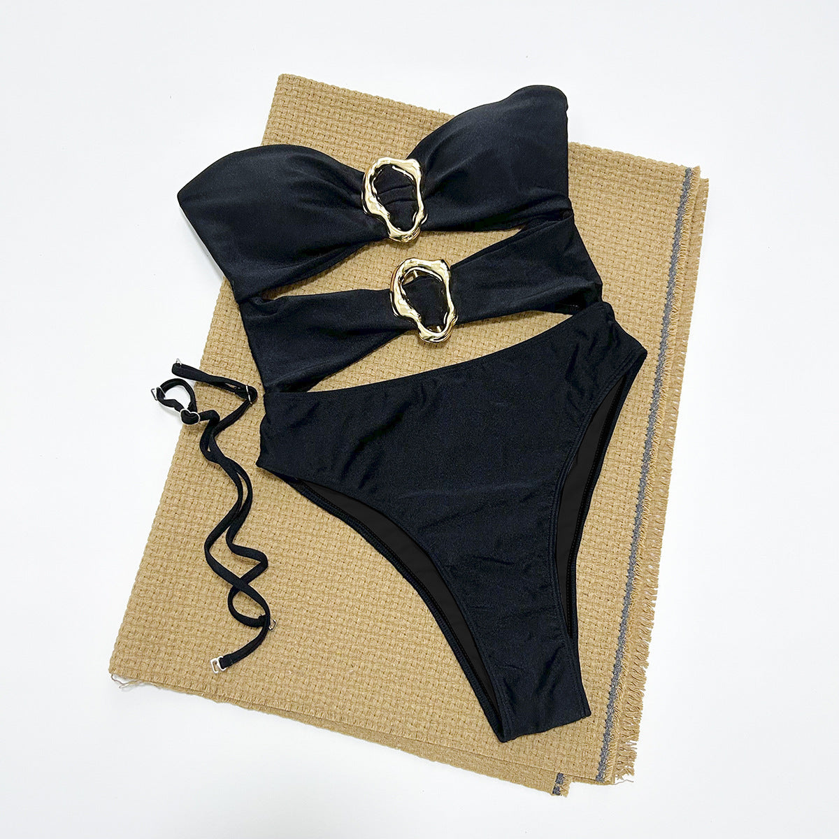 Black bikini set with gold straps on a textured mat