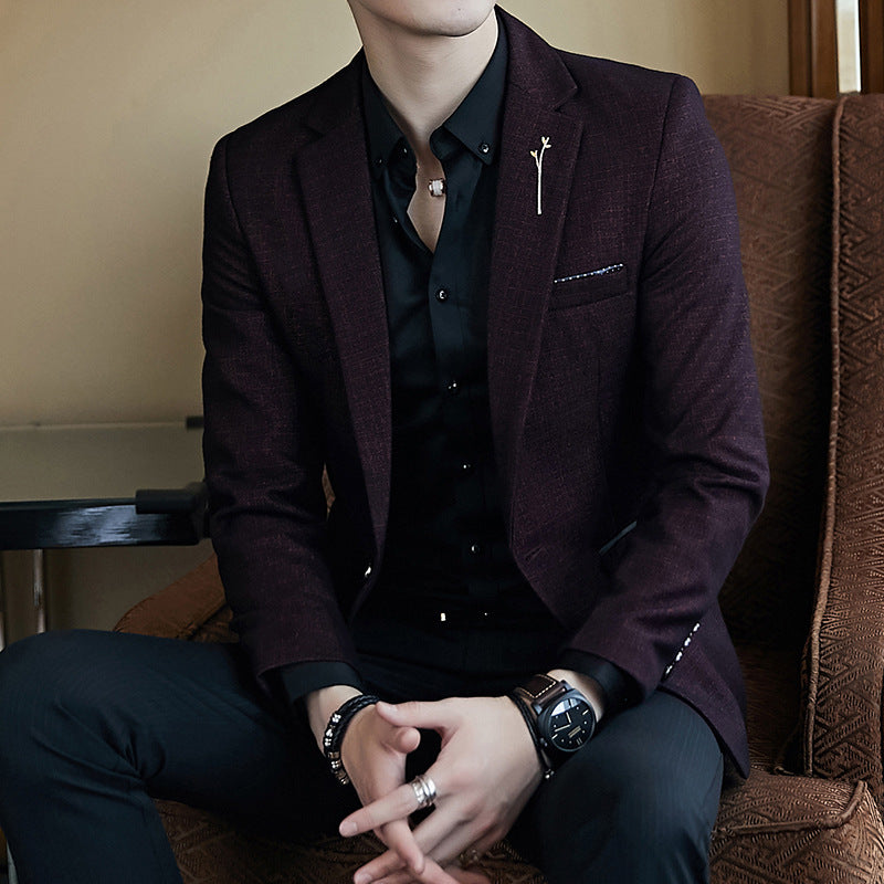 Person wearing a dark suit with a brooch, sitting on a brown couch.