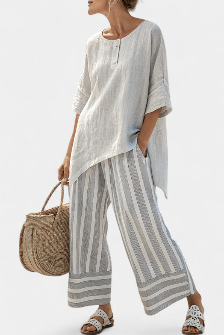 Woman wearing a light-colored outfit with striped pants and holding a woven bag on a white background