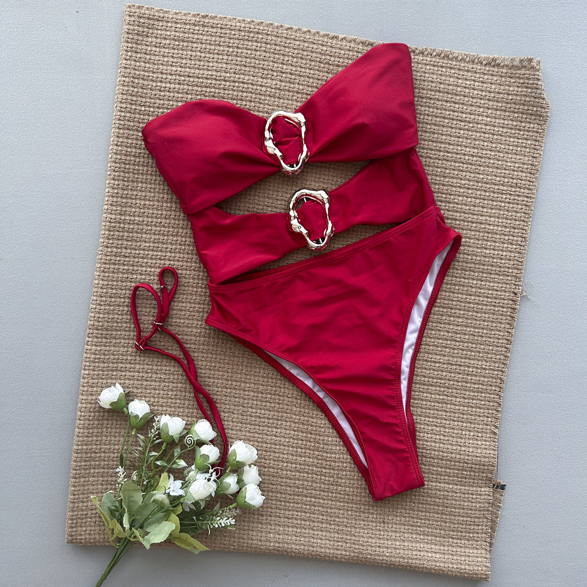 Red bikini set with gold buckles on a textured mat with flowers.