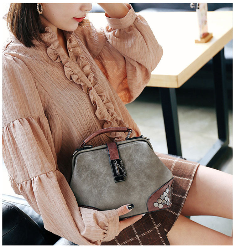 Woman holding a gray handbag with a brown strap in an indoor setting