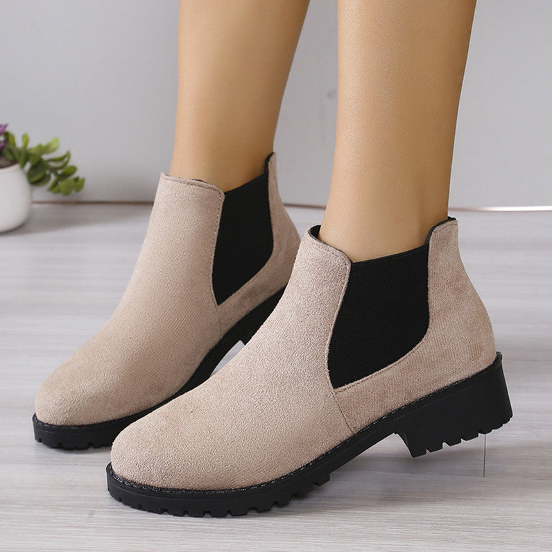 Beige ankle boots with black soles worn by a person on a light wooden floor.