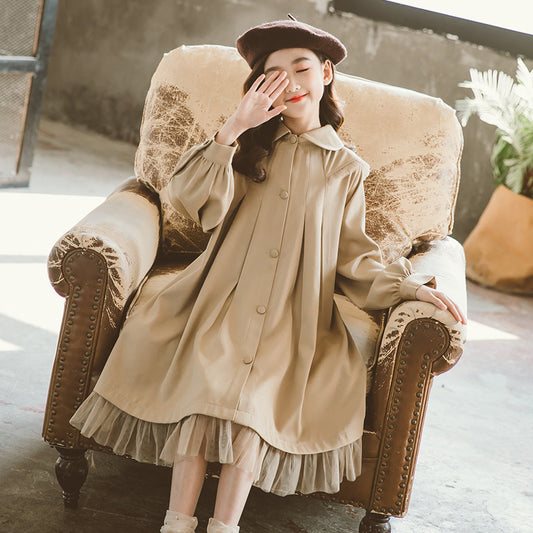 Woman in a beige coat and beret sitting on an ornate armchair.