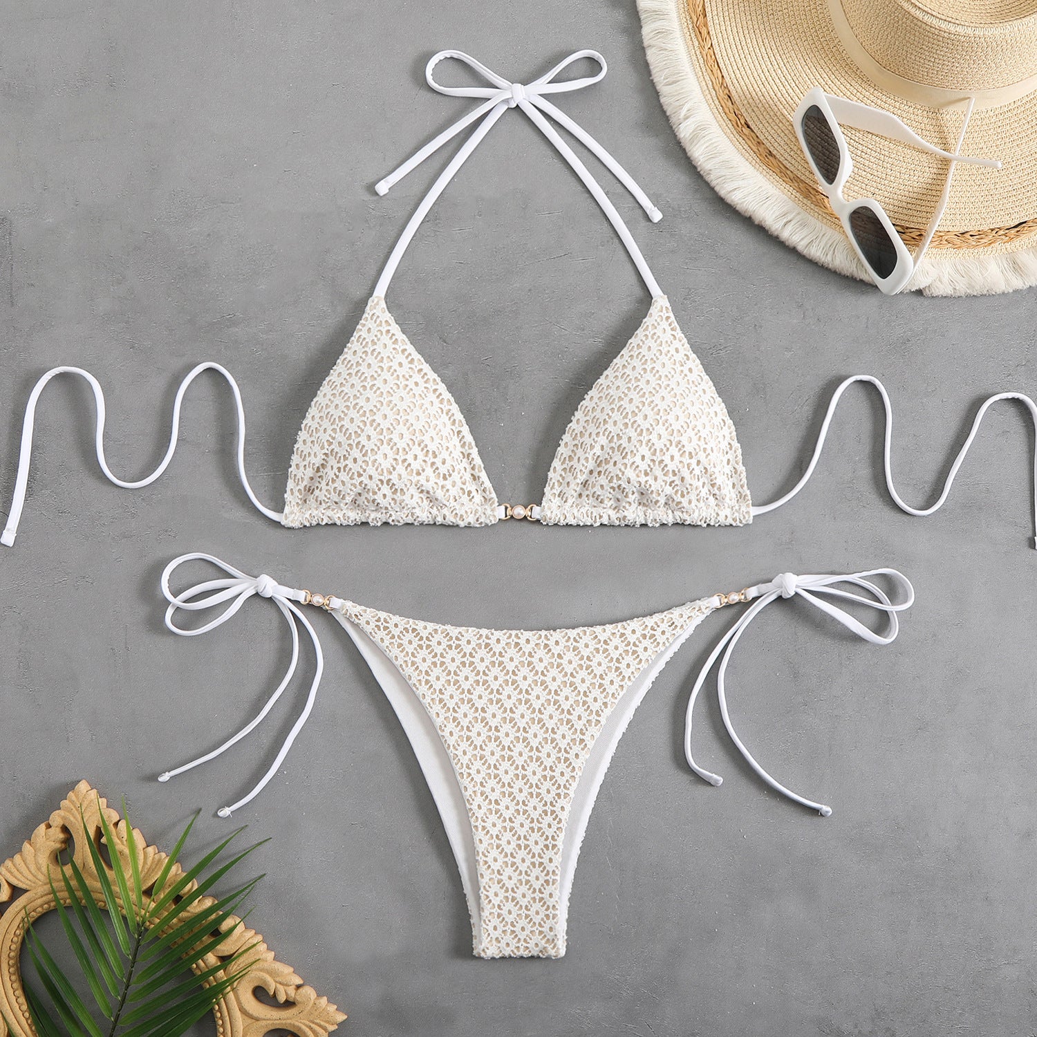White lace bikini set with matching straps on a gray surface, accompanied by a hat and sunglasses.