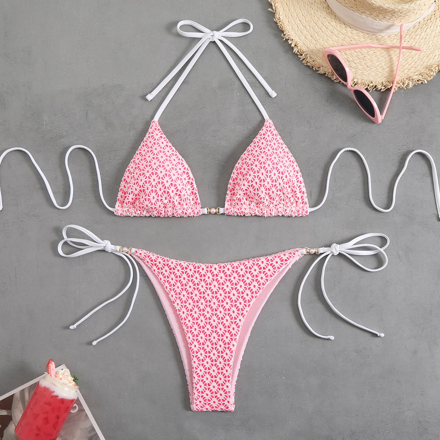 Pink floral bikini set on a gray surface with sunglasses and a hat.