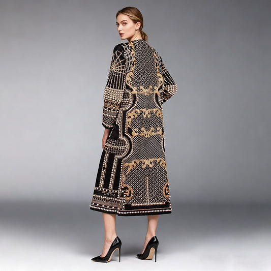 A woman modeling a long black open-front cardigan with intricate gold and beige geometric and floral patterns, shown from a three-quarters back view against a gray studio background.