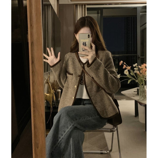 Person wearing a brown blazer and blue jeans sitting in a room with a vase of flowers on a table.