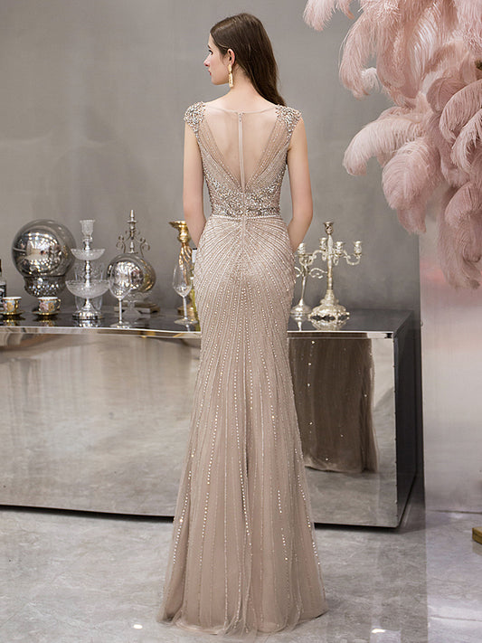 Woman in a beaded evening gown standing in an elegant room with decorative elements.