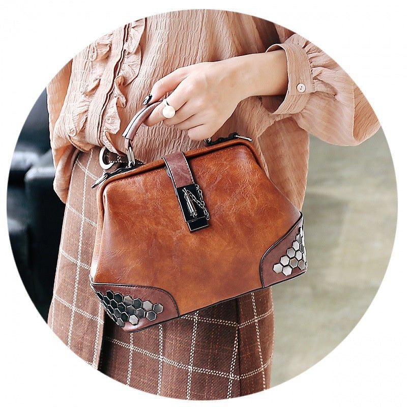 Brown leather handbag with decorative elements held by a person wearing a plaid skirt.