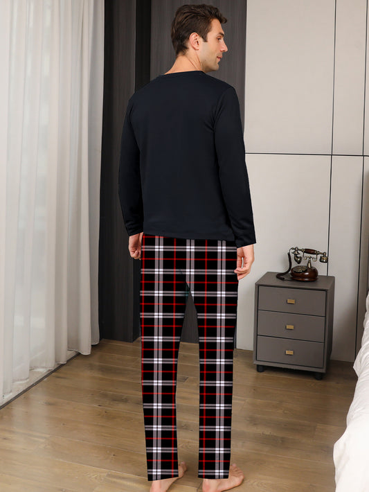Man wearing black long-sleeve top and plaid pants in a bedroom setting.