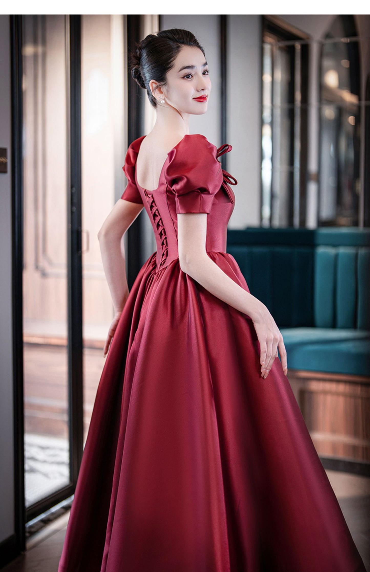 Woman in a red evening gown standing in an elegant interior setting.